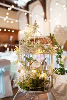 a birdcage filled with flowers and greenery sitting on top of a table