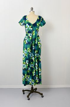 "Info: ♥ Circa: 60s ♥ Label: Ui-Maikai ♥ Color: Blue, green, white ♥ Material: Cotton ♥ Condition: Mint deadstock condition. Details: ♥ Amazing NOS 60s era Hawaiian dress by Ui-Maikai, complete with original tags! ♥ Cotton material in shades of blue, green, and white, featuring a hibiscus floral print ♥ Interior waist has two attached ties to create extra cinch ♥ Elegant fabric draping at back ♥ Unlined ♥ Back center zipper closure Measurements: Bust: 31\"-32\" Waist: 33\" (uncinched) Hips: 47\" Green Hawaiian V-neck Dress, Green Hawaiian Floral Print Dress, Retro Green Floral Print Maxi Dress, Green Hawaiian Maxi Dress For Spring, Green Retro Maxi Dress With Floral Print, Fitted Green Maxi Dress With Tropical Print, Green Fitted Tropical Dress, Fitted Tropical Green Dress, Fitted Green Tropical Dress