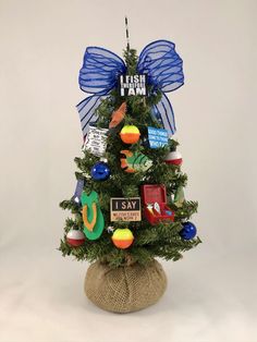 a small christmas tree decorated with ornaments and blue bow on it's top, in front of a white background