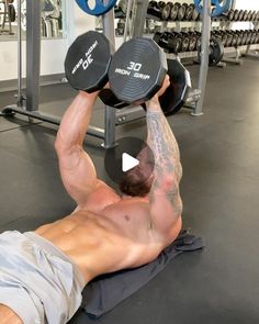 a shirtless man laying on top of a gym floor holding two dumbbells