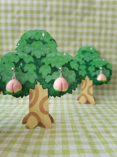 three small trees with pink and green earrings on them sitting on a checkered table cloth