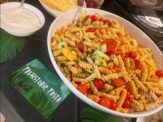 a bowl of pasta with tomatoes, cucumbers and other toppings on a table