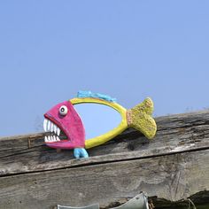 a fish shaped mirror sitting on top of a wooden fence