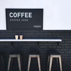 three stools in front of a black brick wall with a sign above it that says coffee served here