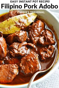 a bowl filled with meat and sauce on top of a white table next to a spoon