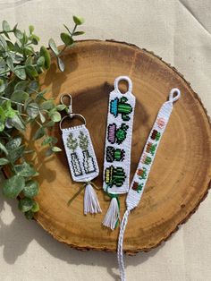 two cross stitch keychains sitting on top of a tree stump next to a plant