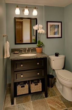 a white toilet sitting next to a sink in a bathroom under two framed pictures on the wall