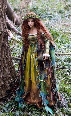 a woman with long red hair and green dress standing next to a tree in the woods