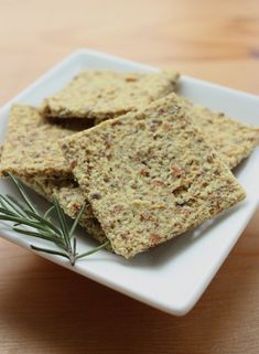 some crackers on a white plate with a sprig of rosemary next to it