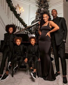 a group of people standing next to each other in front of a christmas tree and piano