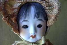 an old doll wearing a bonnet and dress with blue eyes is posed for the camera