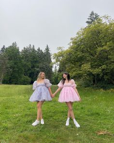 two girls in dresses are walking through the grass with their arms around each other while holding hands