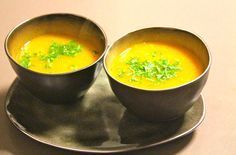 two bowls of soup sit on a silver plate, with garnishes in them