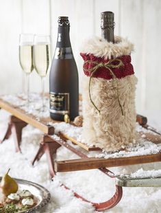 a wine bottle wrapped in red ribbon sitting on top of a sled filled with snow