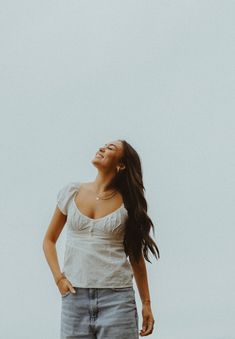 a woman standing in front of a white sky with her hands on her hips looking up