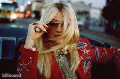 blond woman in red jacket sitting on the back of a car