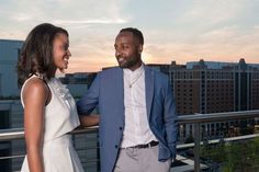 a man and woman standing next to each other on top of a roof in front of buildings