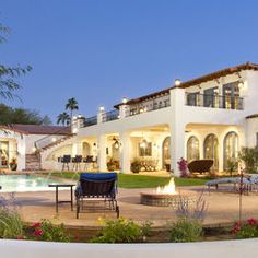 a large white house with a pool in the front yard and patio furniture around it