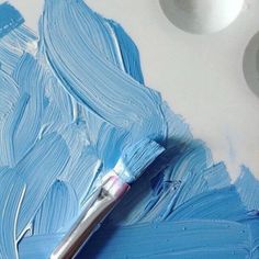 a paintbrush sitting on top of a white table next to some blue and white paints