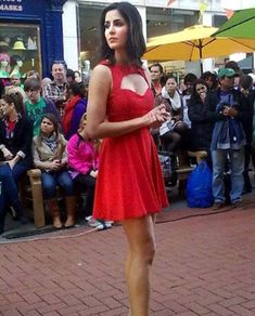 a woman in a red dress is standing on a brick sidewalk while people watch from the street