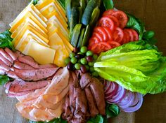 a platter filled with meat, cheese and veggies on top of a table