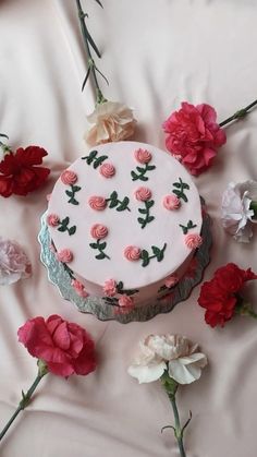 a white cake with pink and red flowers on it sitting on a table next to other flowers