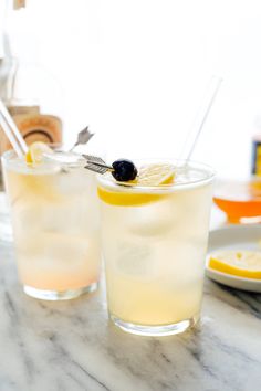 two glasses filled with lemonade sitting on top of a marble table next to plates