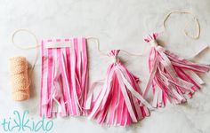 pink and white paper tassels are hanging from twine on a marble surface