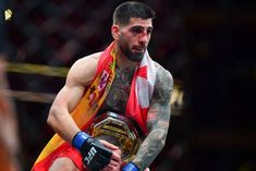 a man with tattoos on his arm holding a wrestling belt and looking at the camera