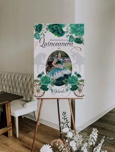 an easel with a poster on it in front of a couch and table next to flowers