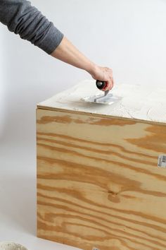 a person holding a remote in their hand over a wooden box