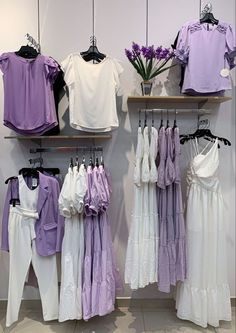 clothes hanging on shelves in a store with purple and white shirts hung up against the wall