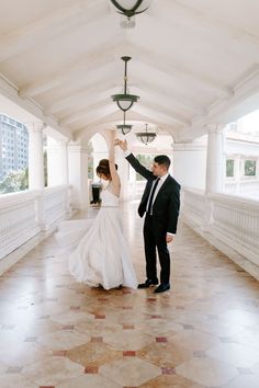 a bride and groom dancing together in an open room with white walls, columns and ceiling