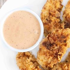 some fried food on a white plate with a bowl of dipping sauce in the middle