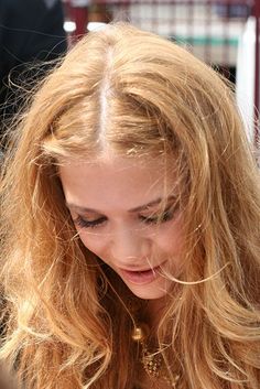 a woman with long blonde hair looking down at her cell phone while holding it in her hand