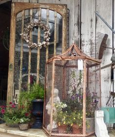 an old birdcage is sitting on the porch next to some flowers and plants