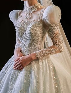 a woman in a wedding dress with a veil on her head and hands behind her back