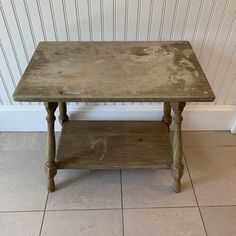 an old wooden table sitting on top of a tile floor next to a white wall