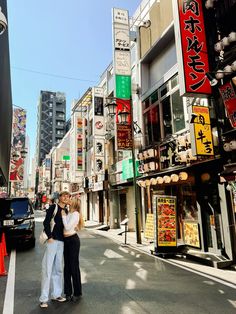 two women standing in the middle of an empty street with buildings and signs on both sides