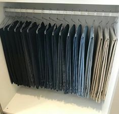 an organized closet with folded shirts and pants hanging on the hooks, in front of a white wall