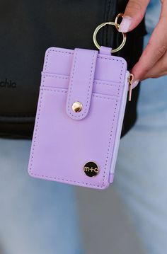 a person holding a purple wallet with a gold keychain on it's side