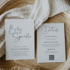 two white wedding cards on top of a wooden table next to a cloth covered blanket