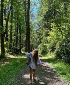 a woman walking down a dirt road in the woods with her back to the camera