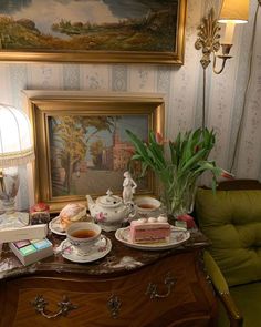 there is a table with tea, cake and other items on it in front of a painting