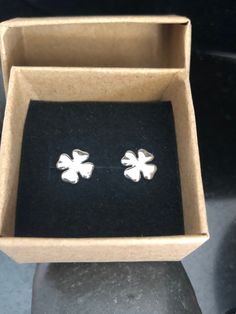 two small silver flower stud earrings in a cardboard box on top of a black surface