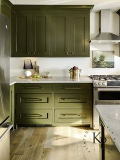 a kitchen with green cabinets and white counter tops, wood flooring and stainless steel appliances