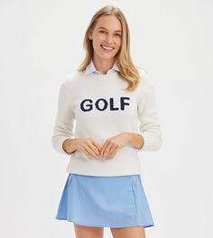 a woman in a white golf sweater and blue skirt poses with her hands on her hips