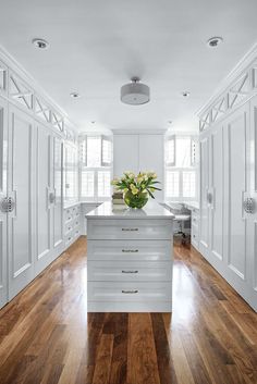 a white kitchen with wooden floors and cabinets in the center is surrounded by large windows