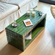 a coffee table made out of tiles with two candles on top and magazines in front