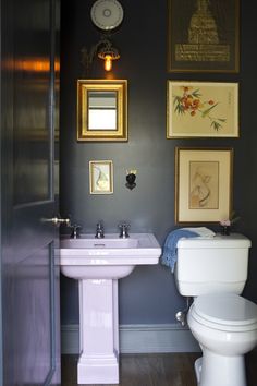 a white toilet sitting next to a sink in a bathroom under pictures on the wall